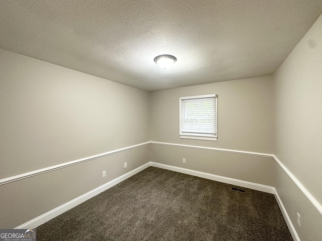empty room with a textured ceiling, baseboards, visible vents, and dark carpet