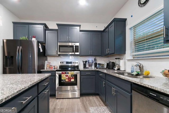 kitchen with decorative backsplash, light stone countertops, a sink, light wood-style floors, and stainless steel appliances