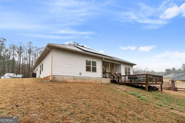 rear view of property featuring a lawn, a deck, and roof mounted solar panels