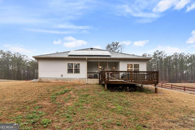 rear view of property featuring roof mounted solar panels, fence, a lawn, and a deck