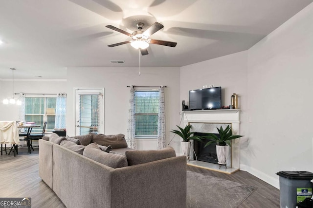 living area with ceiling fan, a fireplace, baseboards, wood finished floors, and visible vents