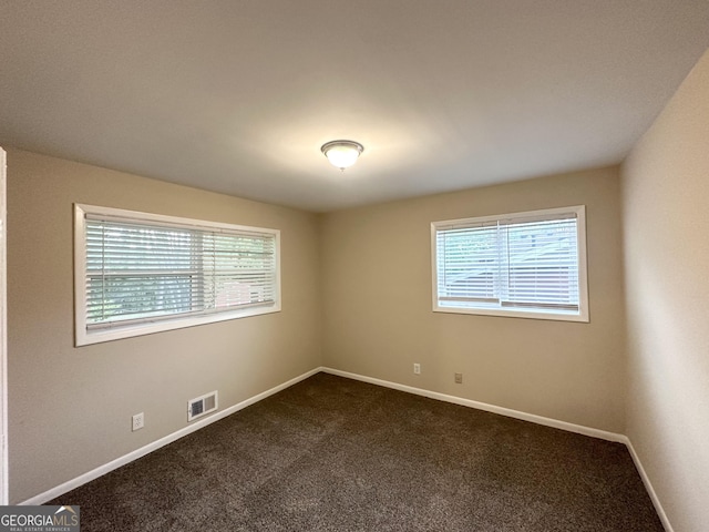 spare room featuring baseboards, dark carpet, and visible vents