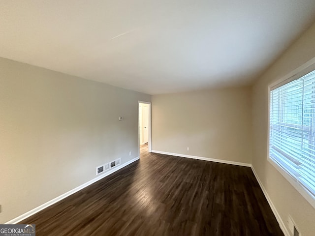 empty room featuring baseboards, visible vents, and dark wood-type flooring