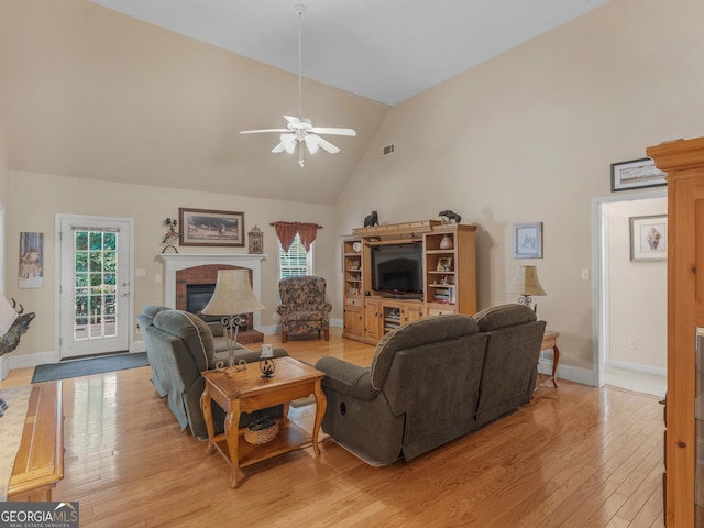 living area with a fireplace, high vaulted ceiling, a ceiling fan, baseboards, and light wood-type flooring