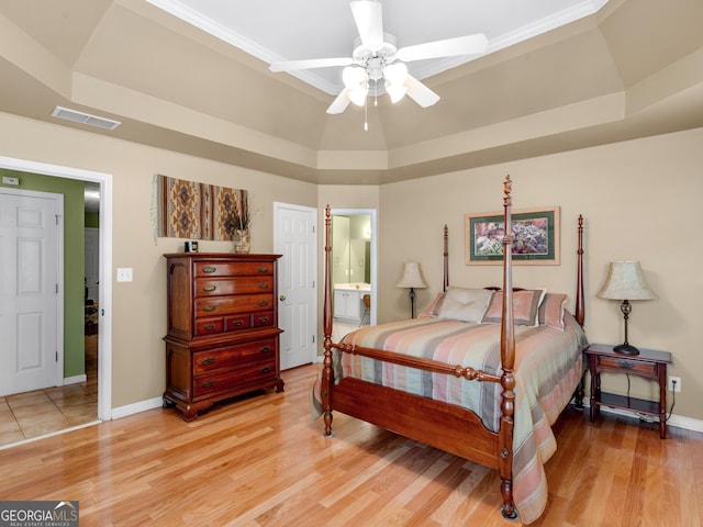 bedroom featuring visible vents, baseboards, a raised ceiling, connected bathroom, and light wood-style flooring