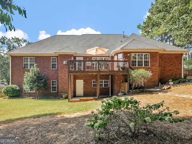 back of property featuring a yard, brick siding, a wooden deck, and roof with shingles