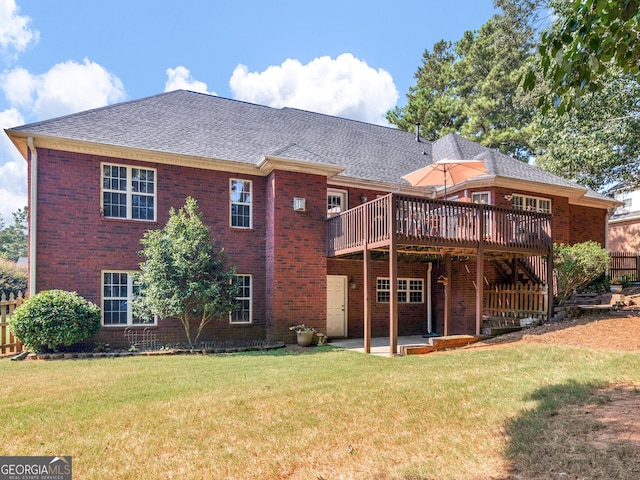 rear view of house featuring a shingled roof, brick siding, a wooden deck, a patio, and a yard