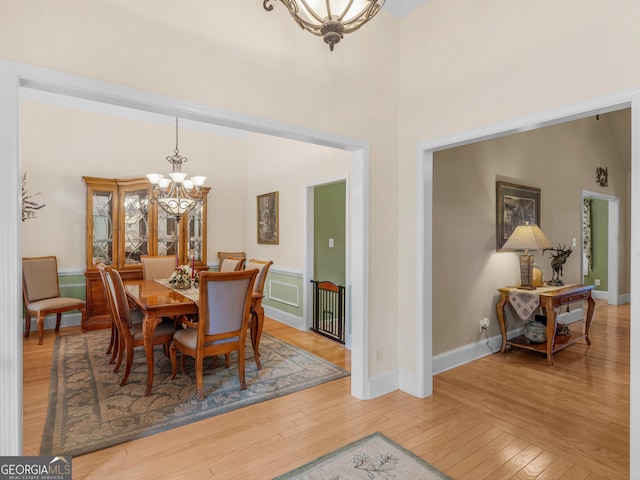 dining area featuring an inviting chandelier, baseboards, light wood-style flooring, and a high ceiling