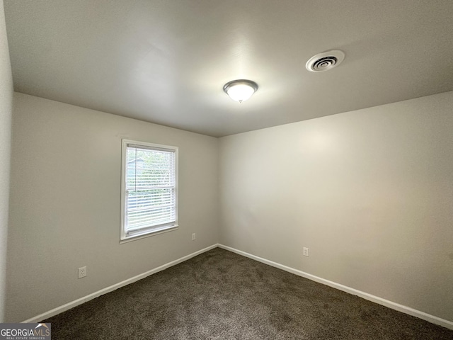 spare room featuring baseboards, dark colored carpet, and visible vents
