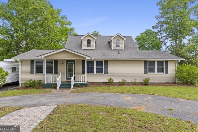 new england style home featuring a porch, a shingled roof, and a front yard