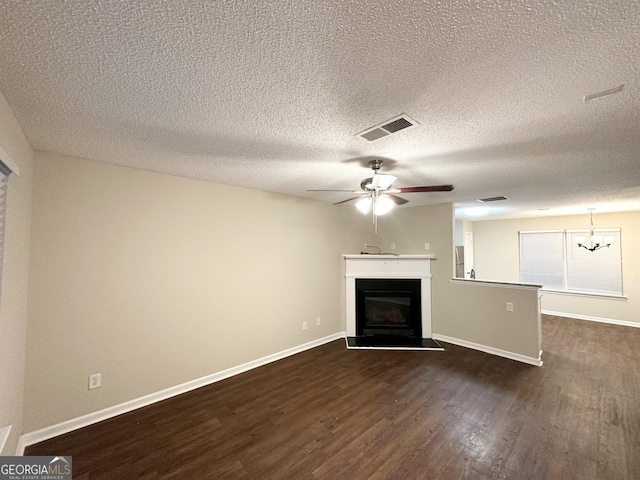 263 Coral Cir, Mcdonough, GA 30253 - unfurnished living room with visible vents, a glass covered fireplace, dark wood-type flooring, a textured ceiling, and ceiling fan with notable chandelier