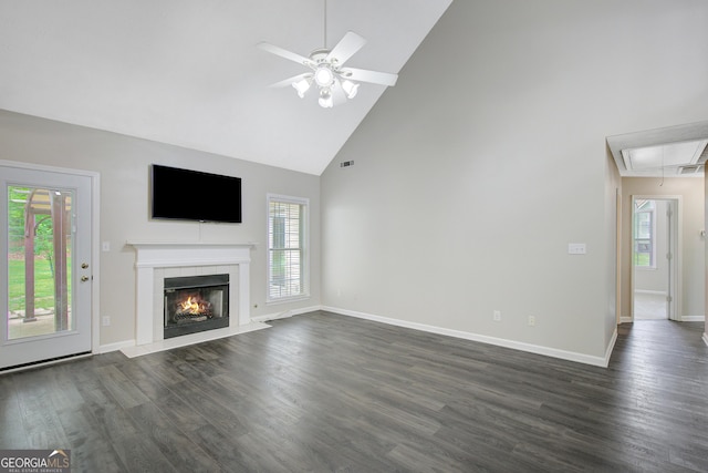 unfurnished living room with a healthy amount of sunlight, high vaulted ceiling, attic access, and dark wood-style floors