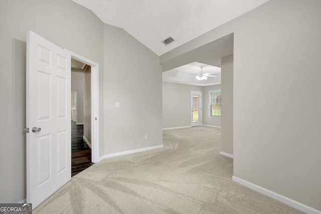 carpeted spare room with baseboards, ceiling fan, vaulted ceiling, and visible vents