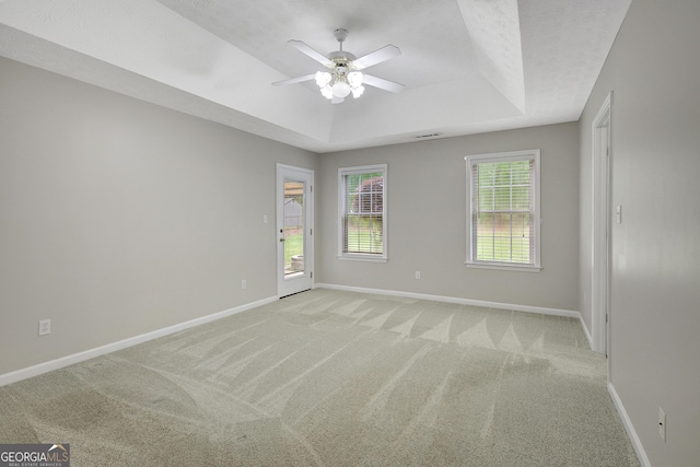 empty room with baseboards, a tray ceiling, and light colored carpet