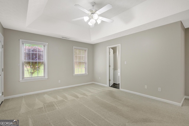 empty room with ceiling fan, light carpet, a raised ceiling, baseboards, and visible vents