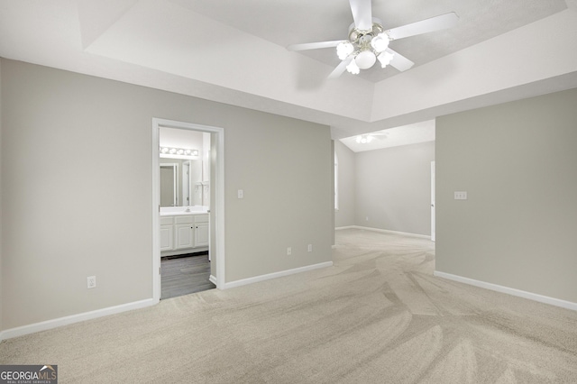 interior space with baseboards, light carpet, a ceiling fan, and a raised ceiling