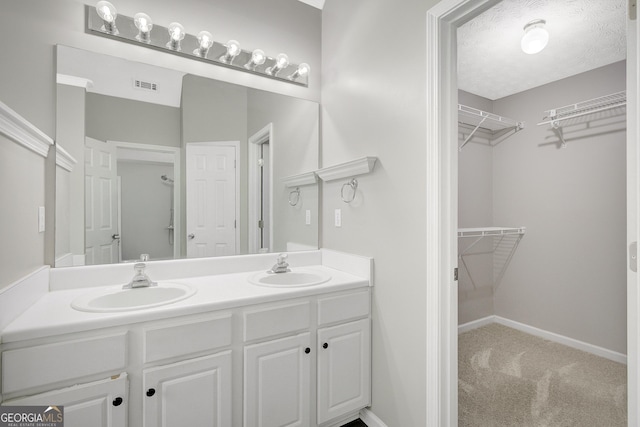 bathroom with double vanity, visible vents, a sink, and a spacious closet