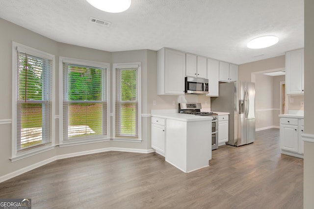 kitchen featuring a textured ceiling, wood finished floors, light countertops, baseboards, and stainless steel appliances