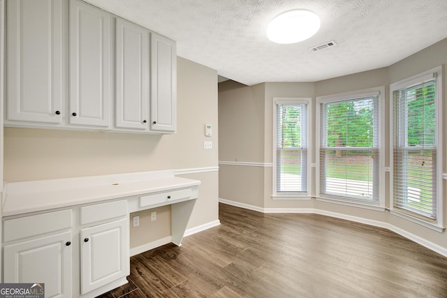 unfurnished office featuring a textured ceiling, baseboards, visible vents, and dark wood-type flooring