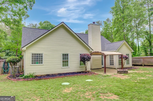 back of house featuring roof with shingles, a patio, a chimney, and a lawn