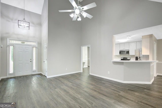 unfurnished living room with baseboards, dark wood-type flooring, ceiling fan with notable chandelier, and high vaulted ceiling