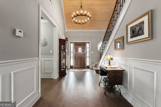 foyer entrance with a decorative wall, a chandelier, stairs, dark wood-type flooring, and a wainscoted wall