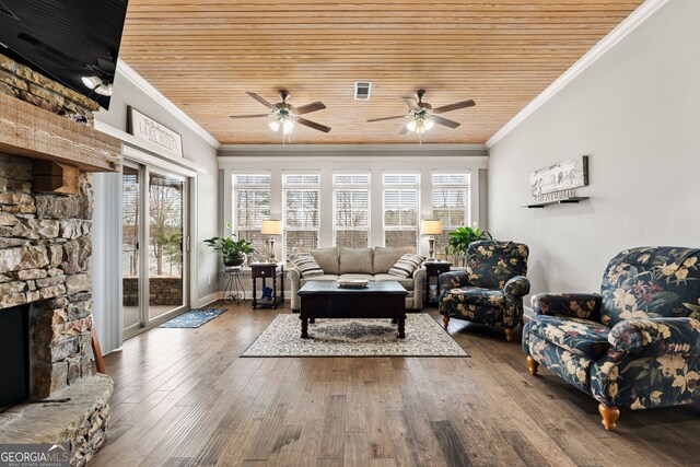 living area with ornamental molding, a ceiling fan, wooden ceiling, wood finished floors, and a stone fireplace