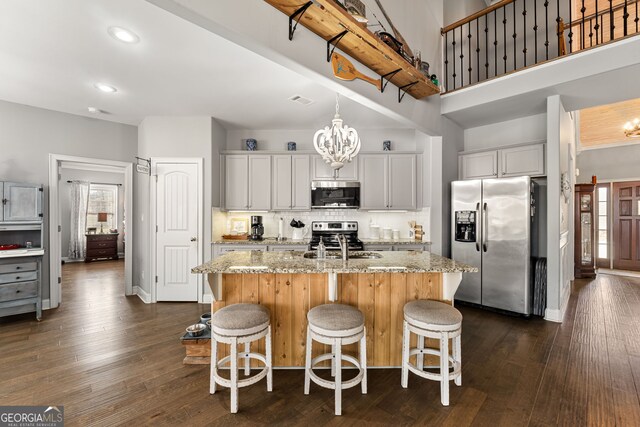 kitchen with appliances with stainless steel finishes, light stone counters, a center island with sink, dark wood-style floors, and a kitchen bar