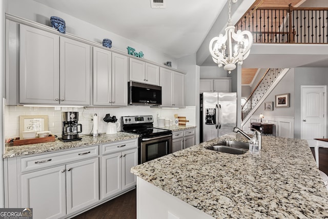 kitchen with appliances with stainless steel finishes, a sink, a chandelier, dark wood finished floors, and light stone counters