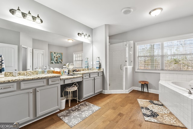 bathroom with a stall shower, wood finished floors, vanity, and a bath