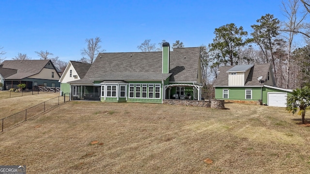 rear view of house featuring a sunroom, a chimney, roof with shingles, a garage, and an outbuilding