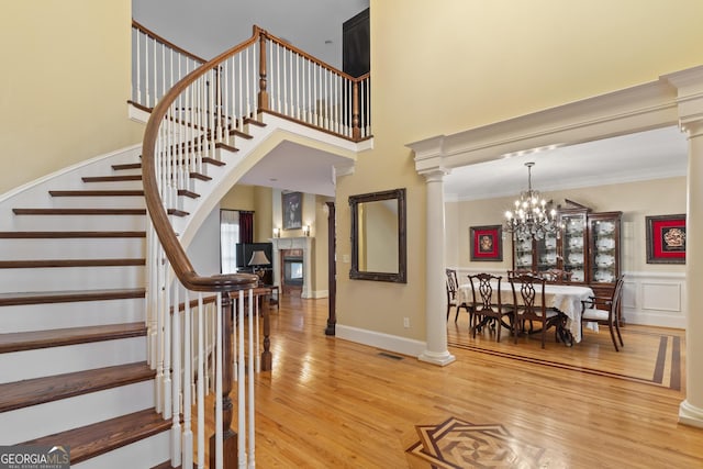 stairway with decorative columns, wood finished floors, a high ceiling, a notable chandelier, and ornamental molding