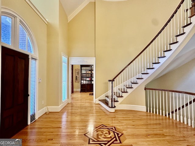 entryway with wood finished floors, stairway, high vaulted ceiling, baseboards, and ornamental molding