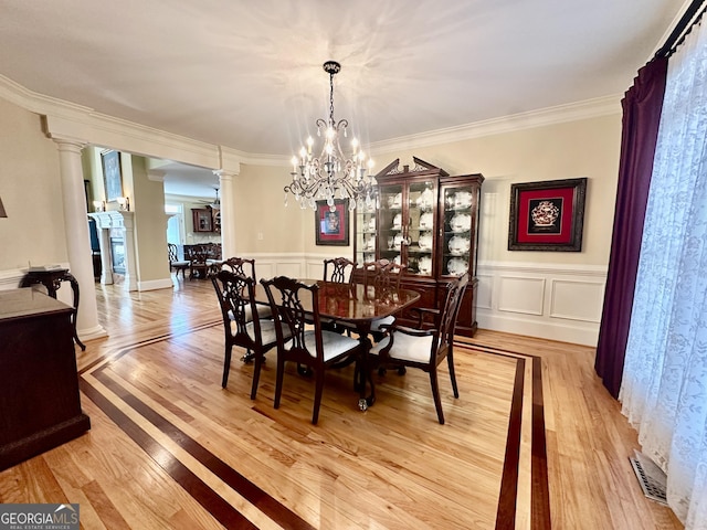 dining room featuring crown molding, ornate columns, an inviting chandelier, and light wood-type flooring