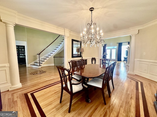 dining space with ornamental molding, stairs, a decorative wall, ornate columns, and light wood finished floors