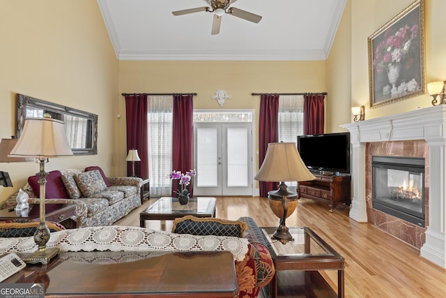living room with a ceiling fan, ornamental molding, a tiled fireplace, and wood finished floors