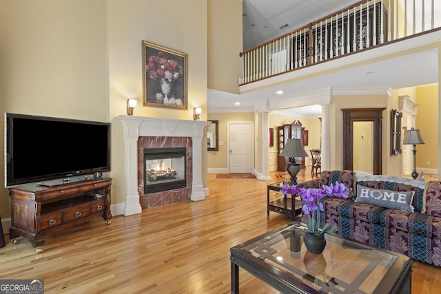 living area with a high ceiling, a fireplace, wood finished floors, ornate columns, and ornamental molding