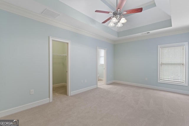 unfurnished bedroom featuring visible vents, ornamental molding, a walk in closet, light colored carpet, and a tray ceiling