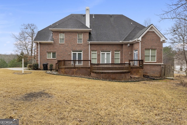 back of house with brick siding, a lawn, a wooden deck, and roof with shingles