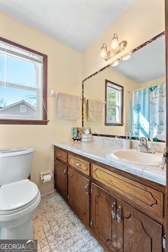 full bath with toilet, a textured ceiling, baseboards, and vanity