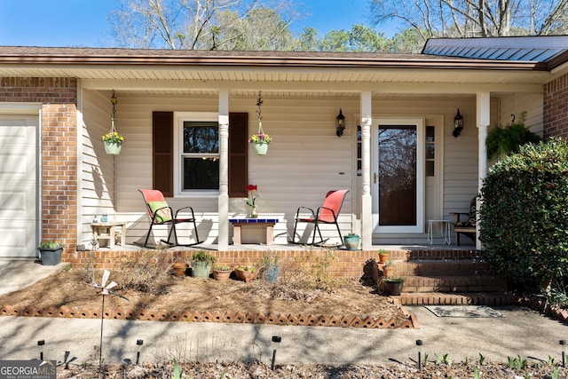 view of exterior entry with a garage, covered porch, and brick siding