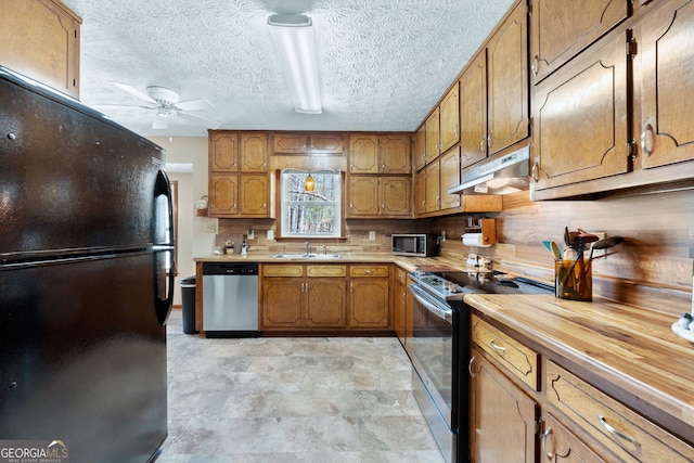 kitchen with brown cabinetry, a sink, under cabinet range hood, and stainless steel appliances