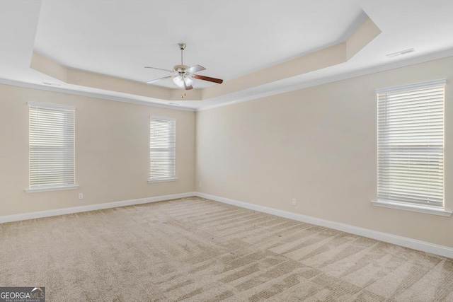 unfurnished room featuring a ceiling fan, a tray ceiling, light carpet, and baseboards