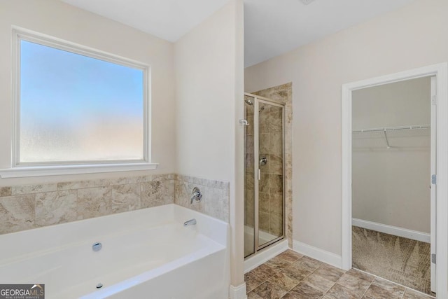 bathroom with baseboards, a walk in closet, a bath, and a shower stall