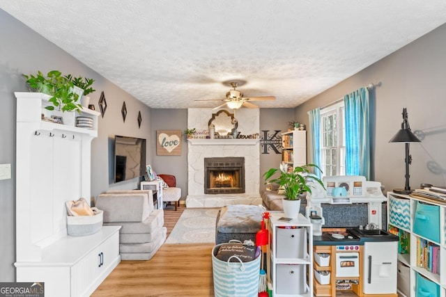 living room featuring a fireplace, a ceiling fan, light wood-type flooring, and a textured ceiling