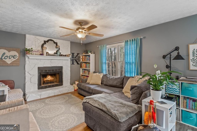living area with a stone fireplace, a textured ceiling, ceiling fan, and wood finished floors