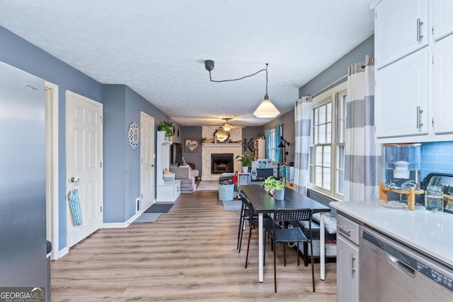 dining room featuring a large fireplace, baseboards, light wood-type flooring, and a textured ceiling