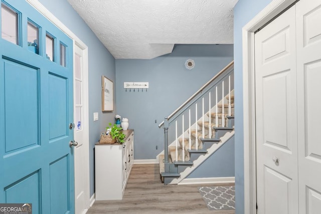 entryway featuring baseboards, a textured ceiling, light wood-style flooring, and stairway