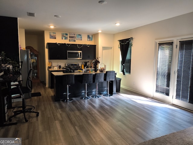 kitchen featuring visible vents, a breakfast bar area, dark wood-type flooring, dark cabinets, and appliances with stainless steel finishes