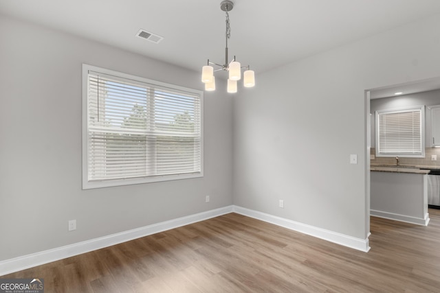 unfurnished dining area with visible vents, light wood-style flooring, baseboards, and a chandelier
